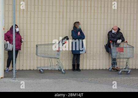 Toscana, Italie 03/27/20 - les clients portant des masques de protection contre les coronavirus en ligne avec des chariots, debout contre un mur blanc. Les personnes qui discutent Banque D'Images