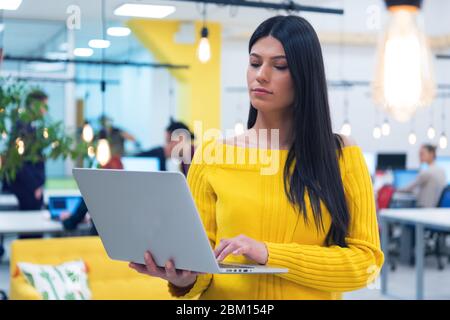 Portrait d'une jeune femme d'affaires décontractée et heureuse debout avec un ordinateur portable sur son lieu de travail dans un espace de travail moderne. Banque D'Images