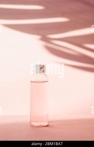Bouteille en plastique avec de l'eau rose rose sur un fond pastel avec ombre tropicale d'une feuille de palmier. Toner et toner transparents pour hydrater et nettoyer la peau. Eau micellaire ou mousse nettoyante. Banque D'Images
