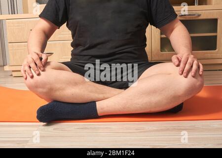 fat homme caucasien assis en position lotus sur le tapis de quarantaine de fitness à la maison Banque D'Images