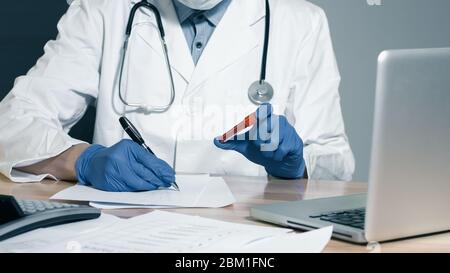 Main d'un médecin tenant un flacon d'échantillon de sang et écrivant dans des dossiers. Banque D'Images