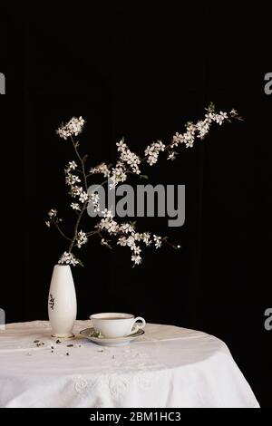 Table noire et blanche en ambiance printanière. Branche d'arbre en fleur dans un vase et une tasse de thé sur une table blanche Banque D'Images