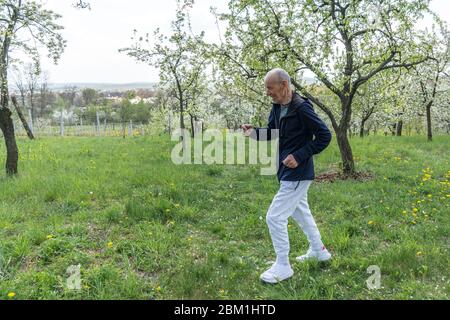 Retraité senior souriant habillé de vêtements de sport élégants jogging dans le parc en fleurs Banque D'Images