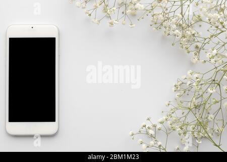 Vue de dessus téléphone portable avec écran vierge avec fleurs sur fond blanc. Cadre à fleurs avec espace pour copier Banque D'Images