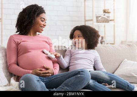 Adorable très petite fille mettant des chaussures de petite taille sur le ventre de maman enceinte Banque D'Images