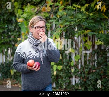 Une femme qui goûtant une pomme fraîche à l'extérieur. Elle tient deux pommes dans ses mains et elle sourit avec joie. Banque D'Images