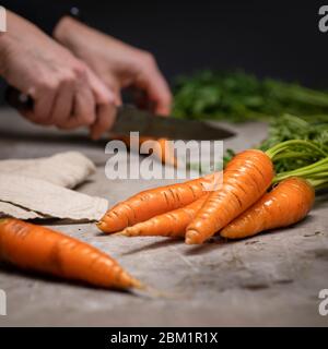 Les femmes coupantes des carottes sur une planche à découper grise. Concentrez-vous sur les carottes à l'avant, l'arrière-plan est sombre. Banque D'Images