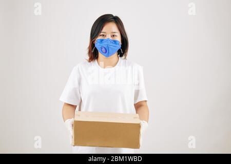 Portrait de la jeune femme asiatique dans un masque médical et des gants en caoutchouc tenant une boîte en carton Banque D'Images