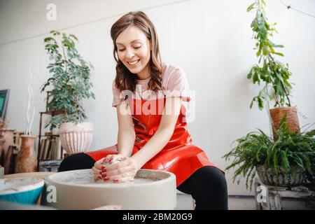 Roue de travail de potier. Bonne jeune femme en tablier rouge sculpte de l'argile Banque D'Images