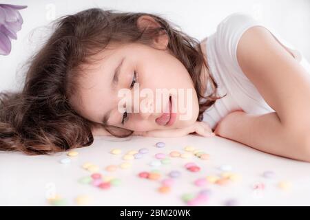 Enfants et chocolat. Une fille gaie joue et mange des bonbons ronds multicolores au chocolat sur un fond clair.fille joyeuse avec des bonbons. Banque D'Images