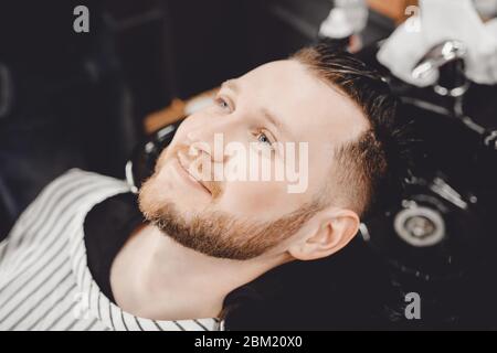 Un client masculin lave son coiffeur et sourit, coiffant avec élégance Banque D'Images