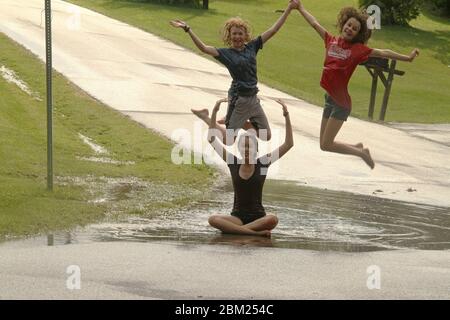 Jeunes filles jouant dans une grande flaque de sol après une forte pluie Banque D'Images