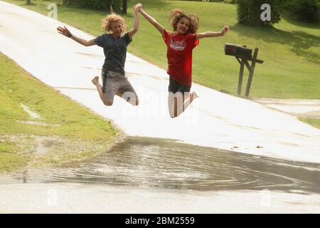 Jeunes filles jouant dans une grande flaque de sol après une forte pluie Banque D'Images