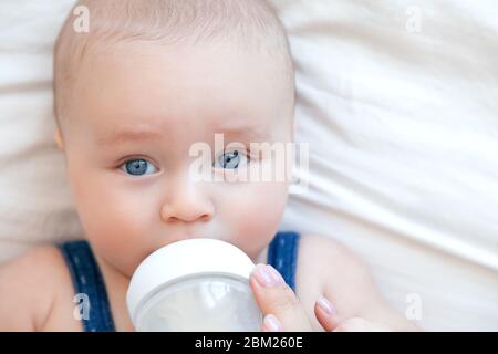 Magnifique bébé mangeant du lait au biberon dans la chambre blanche arrière-plan blanc Banque D'Images