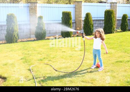 Petite fille avec un tuyau dans ses mains arroser une pelouse verte Banque D'Images