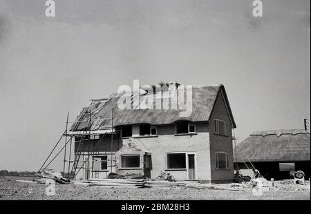 Années 1960, historique, une nouvelle maison de deux étages en cours de construction dans la campagne, avec un toit de chaume sur la maison et le garage, Angleterre, Royaume-Uni. La plupart des bâtiments avec des toits de chaume sont des cottages ruraux traditionnels en pierre, et donc avoir un tel toit sur une maison plus conventionnellement construite à deux étages est inhabituel. Banque D'Images