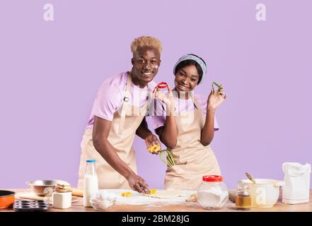 Jolie petite amie africaine américaine et petit ami faisant des biscuits sur fond lilas Banque D'Images