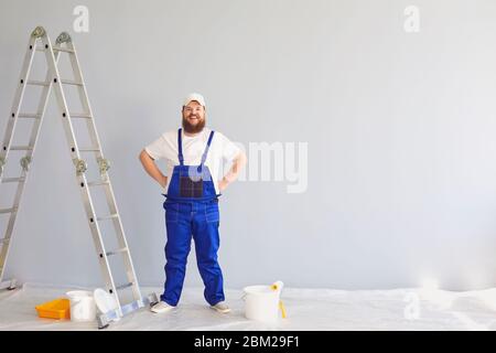 Peinture peintre. Drôle de graisse barbu maison de peintre avec un patineur à roulettes debout peintures dans le fond. Peinture réparation de mur de décorateur à la maison Banque D'Images