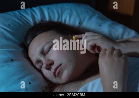 Jeune femme mettant des bouchons d'oreille dans ses oreilles pour la réduction du bruit avant le sommeil, l'insomnie Banque D'Images