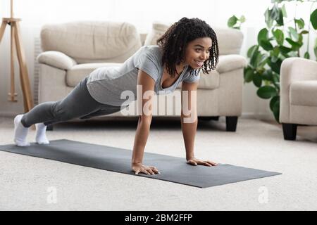Entraînement domestique. Jeune sportive Black femme faisant de l'exercice de planche à la maison Banque D'Images