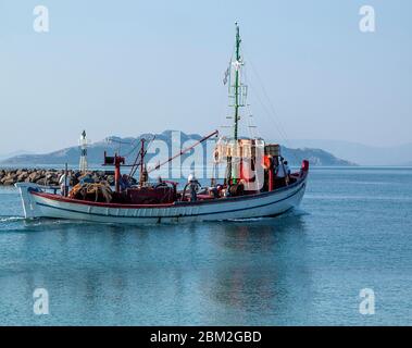 Bateau de pêche quittant le port de la ville d'Aegina lors d'une journée calme en été avec la petite île grecque d'Agistri en arrière-plan, Golfe Saronique, Grèce Banque D'Images