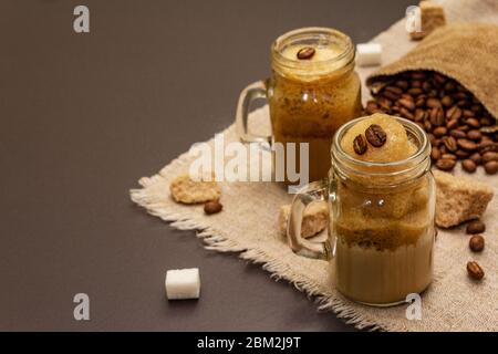 Café Dalgona dans un pot de maçon. Boisson fouettée au café coréen. Boisson de quarantaine, sucre et grains de café tendance sur fond de béton de pierre noire Banque D'Images