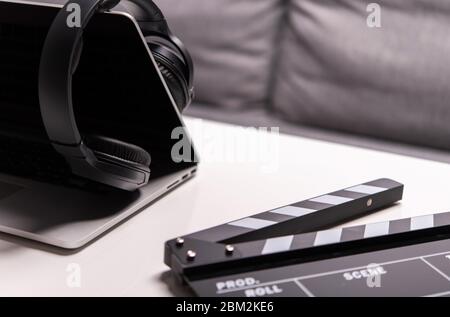 Gros plan sur Clapperboard ordinateur portable ouvert et casque noir sans fil sur table. Banque D'Images