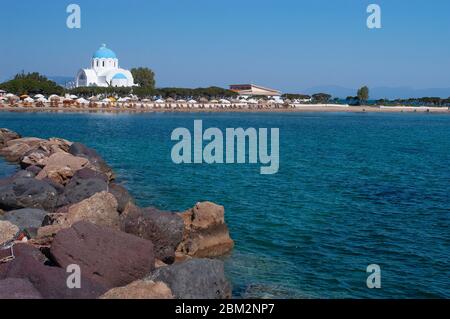 Le front de mer avec plage dans la ville de Skala avec l'église d'Agioi Anargroi sur la petite île grecque d'Agistri, Golfe Saronique, Grèce Banque D'Images