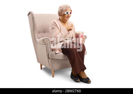 Femme âgée avec des lunettes 3d assise dans un fauteuil en train de manger du pop-corn isolé sur fond blanc Banque D'Images