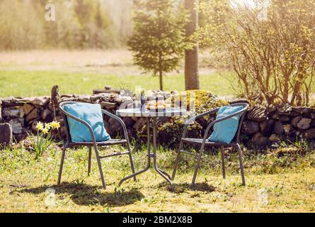 Petite table dans le jardin rural de la maison avec chaises et table pour deux, pâtisseries fraîchement cuites sur la table, matin ensoleillé de printemps. Mur de clôture en pierre empilée Banque D'Images