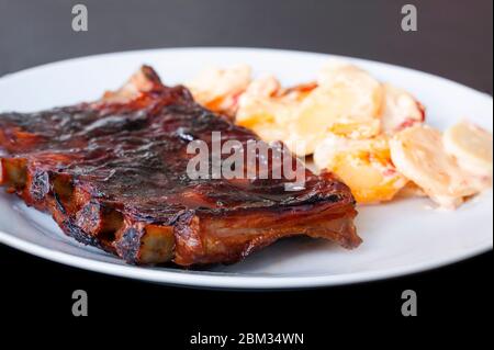 Côtes de rechange grillées et épicées servies au barbecue sur une assiette de paprika aux pommes de terre pétonlées. Gros plan Banque D'Images