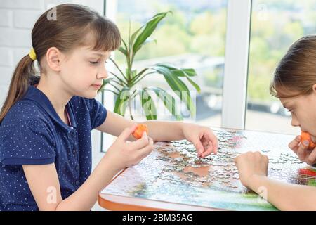 Deux filles collectent des puzzles à la table et mangent des carottes Banque D'Images