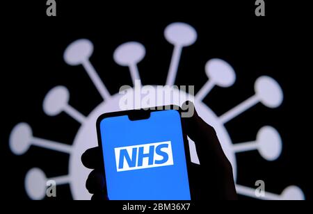 Écran de connexion de l'application NHS sur une silhouette de smartphone tenir dans une main et image du coronavirus COVID-19 sur un arrière-plan flou. Banque D'Images