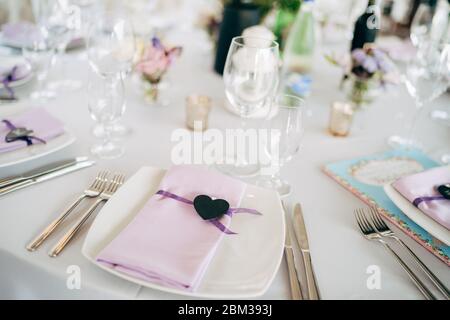 Réception de table de mariage. Assiettes carrées blanches sur une table ronde avec serviettes de table en chiffon rose et coeur noir. Chaises blanches Chiavari, Tiffany. Banque D'Images