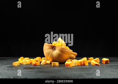 Moitié citrouille avec des morceaux frais sur fond noir. Courge de noyer cendré cru haché, mise au point sélective. Cuisson de plat de légumes Banque D'Images