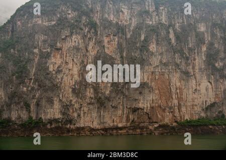 Baidicheng, Chine - 7 mai 2010 : gorge de Qutang sur le fleuve Yangtze. Straigth en bas de la falaise brune avec un feuillage vert et des stalactites plus sombres au-dessus du vert W. Banque D'Images