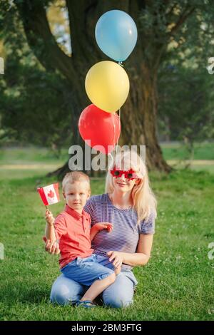 Citoyens famille maman avec enfant célébrant la fête nationale du Canada le 1er juillet. Mère caucasienne avec bébé garçon portant une feuille d'érable drôle Banque D'Images