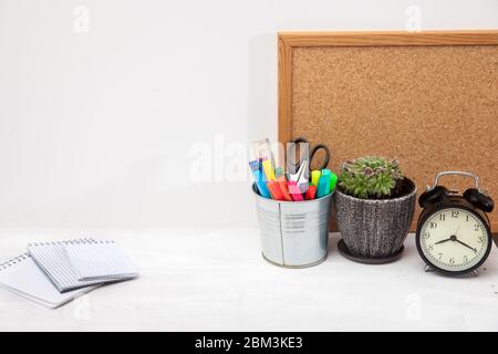 Copier l'espace. Employé de bureau sur le lieu de travail. Réveil, succulent en pot de céramique, tableau d'écriture, seau avec ciseaux, stylos à pointe feutre, règle, trois carnets Banque D'Images