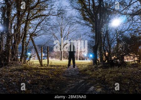 Une silhouette à capuche, silhouetée contre une lumière de rue sur le bord de la ville la nuit Banque D'Images