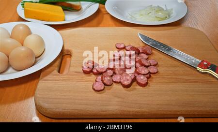 Kit pour une cuisson rapide sur la table de cuisine. Saucisse coupée au couteau sur une planche de bois et divers aliments sur des assiettes Banque D'Images