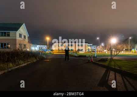 Une silhouette à capuche, taillée contre une lumière de rue sur un domaine d'affaires la nuit Banque D'Images