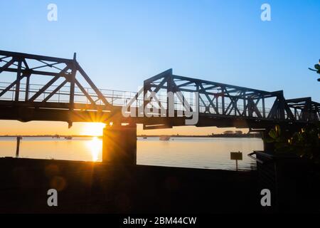 Pont ferroviaire silhoueté par le lever du soleil à travers le port de Tauranga en Nouvelle-Zélande. Banque D'Images