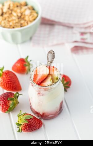 Yaourt blanc fruité dans un pot et fraises sur table blanche. Banque D'Images