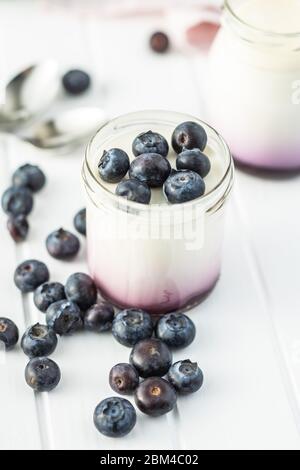 Yaourt blanc fruité en pot et bleuets sur table blanche. Banque D'Images