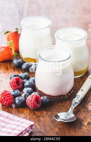 Yaourt blanc fruité en pot et bleuets, framboises, fraises sur table en bois. Banque D'Images