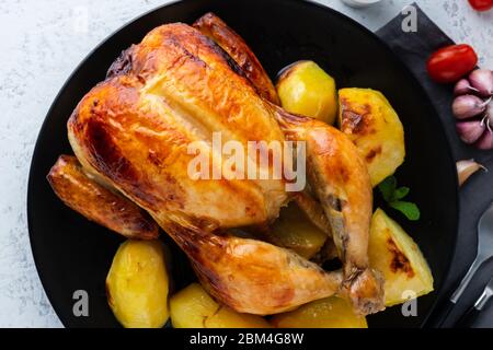 Poulet entier grillé sur une assiette noire sur une table blanche, viande cuite avec des pommes de terre. Vue de dessus, gros plan Banque D'Images