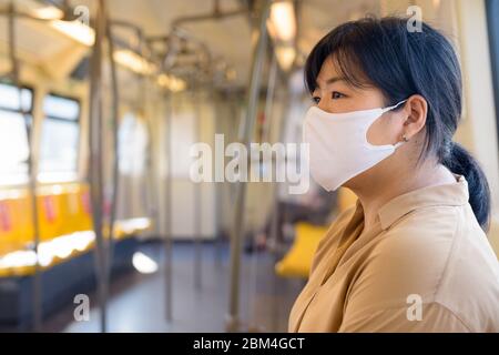 Femme asiatique en surpoids avec masque assis à distance à l'intérieur du train Banque D'Images