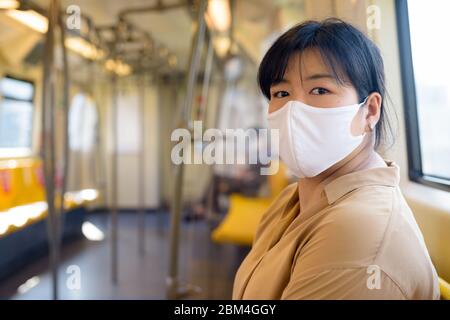 Femme asiatique en surpoids avec masque assis à distance à l'intérieur du train Banque D'Images