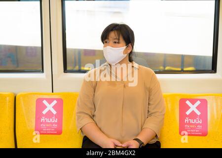 Femme asiatique en surpoids avec masque pensant et assis avec la distance à l'intérieur du train Banque D'Images