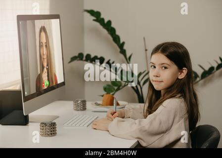 Formation à distance. Une jeune fille avec de longs cheveux étudiant à distance de son professeur de femme en ligne. Un joli enfant apprend une leçon en utilisant une comput de bureau Banque D'Images